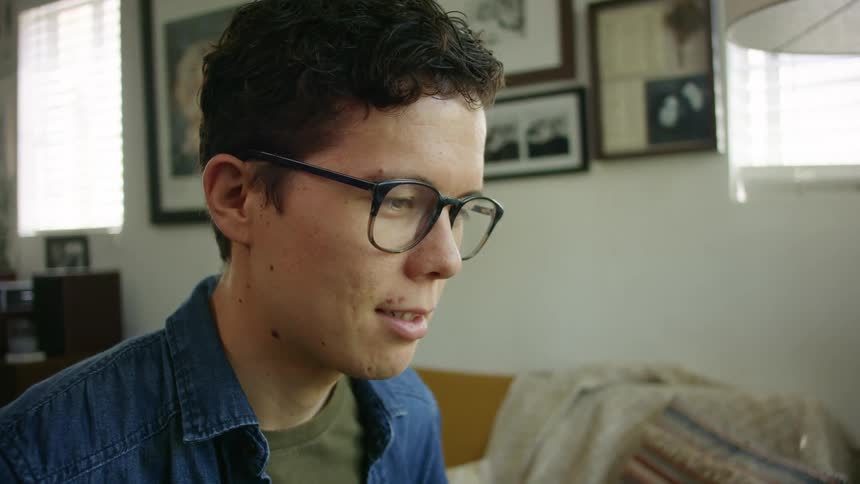 A young man nods while sitting indoors