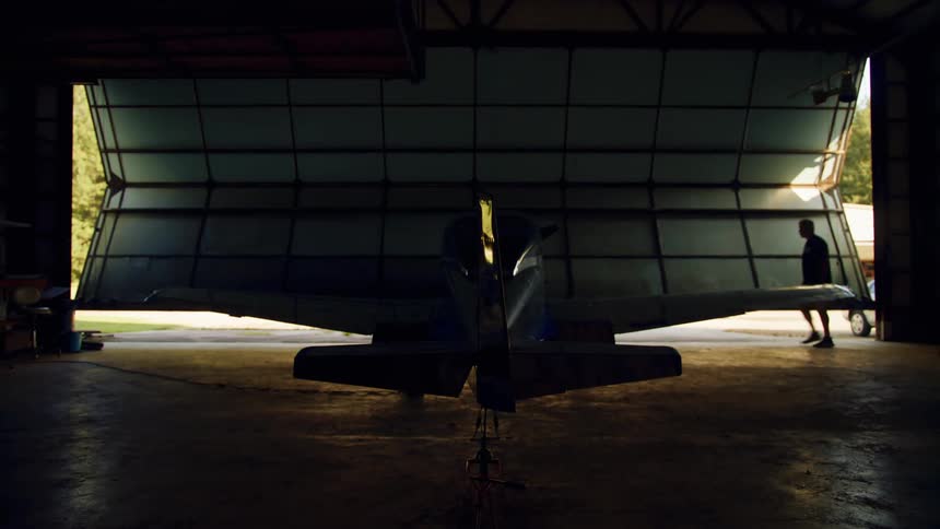 A man walking in a hangar as the door opens with a plane inside