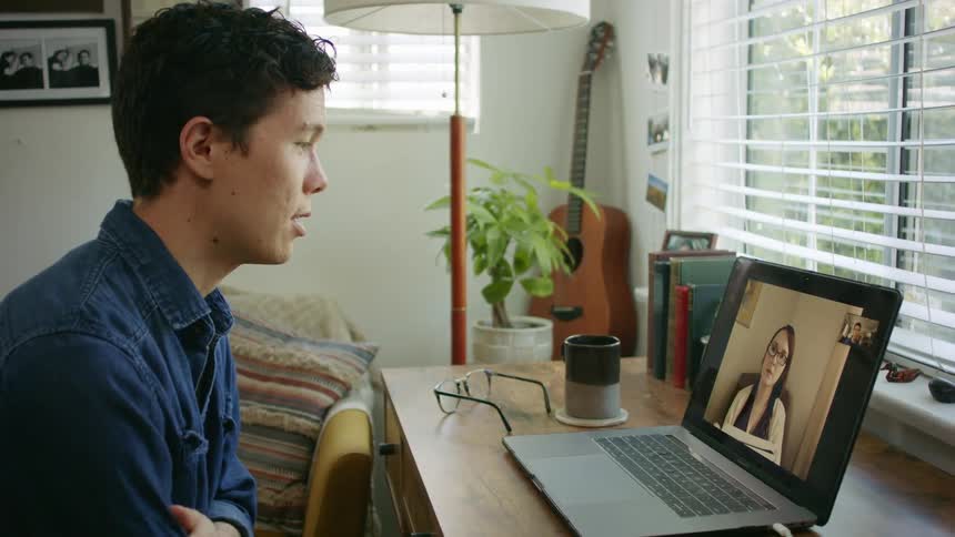 A man sitting at home nervously rubs his arm as he video chats with a woman on his laptop