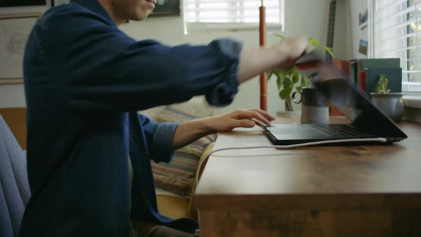 Man sits down on a desk and opens a laptop in the living room at home