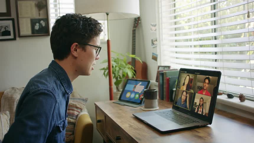A man sitting at home video chats with people on his laptop