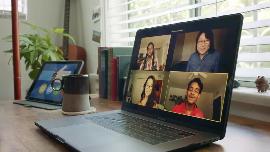A person at home looks at a laptop with four people video chatting on the screen