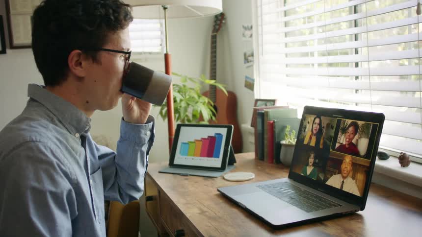 Male drinking coffee while on zoom call with colleagues working remotely