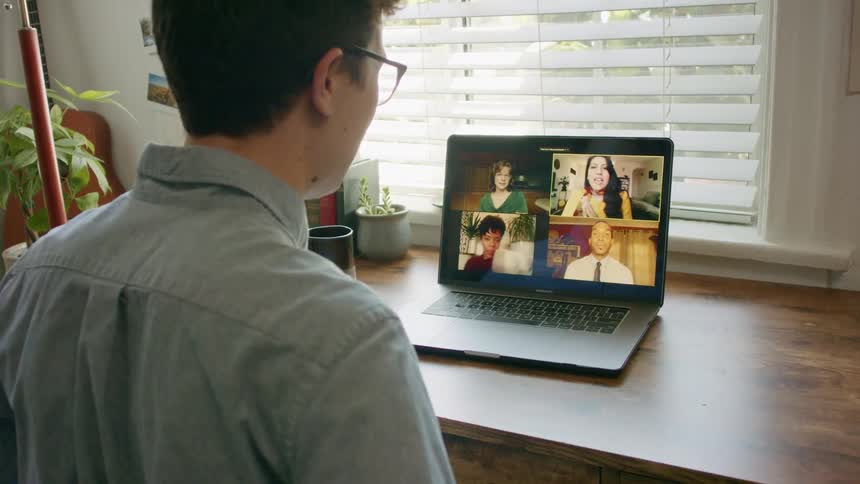 A man sits at his desk at home participating in a video conference with four people on screen