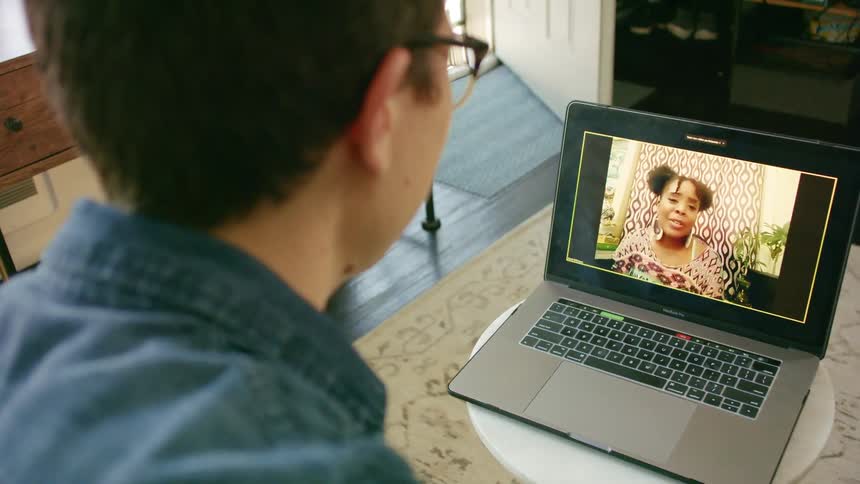 A man sits in front of a laptop having a video call with a woman