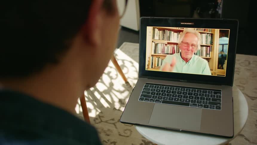 Man with glasses sits and makes a video call on macbook pro with an elderly man in the living room at home