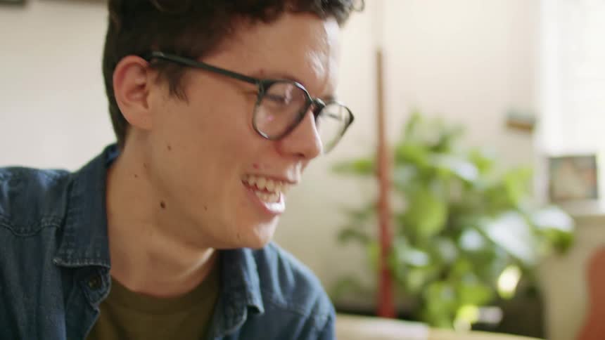 A man with glasses talking with a plant and a window in the background