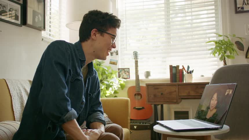 Man talks to woman via video call on laptop while sitting on couch