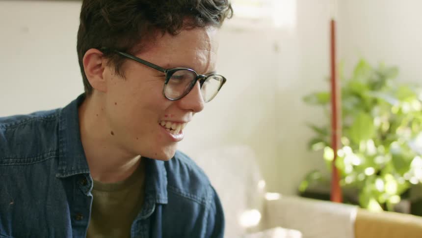 A young man at home laughs and waves