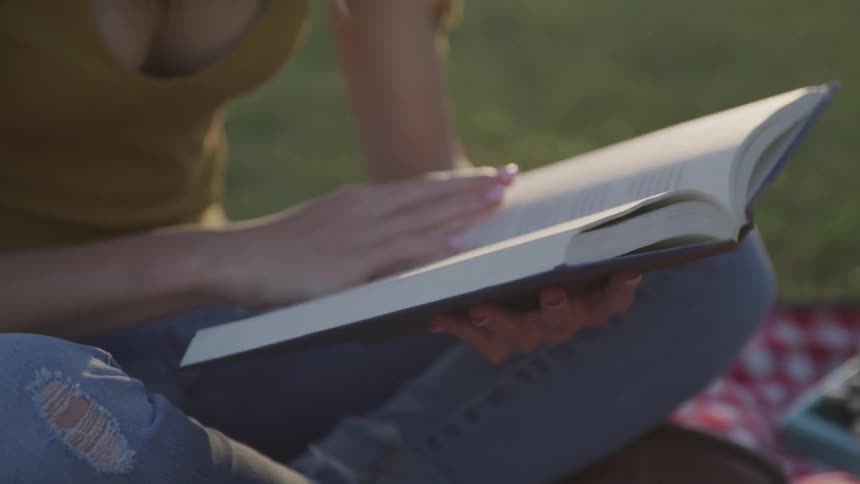 Woman with ripped jeans sits on the grass and reads a book
