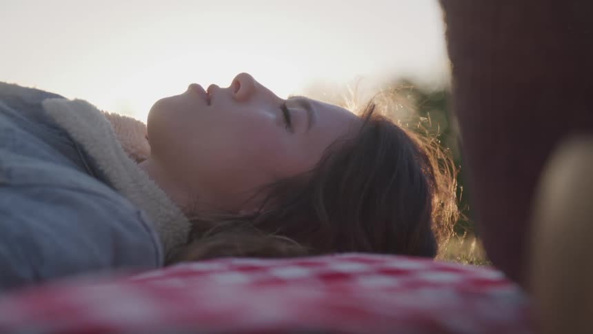 A woman is laying on a checkered blanket in a grassy field and staring up at the sky