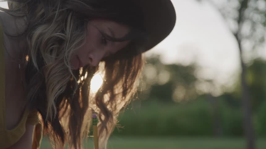 A woman sits in a field outdoors while writing with a pencil