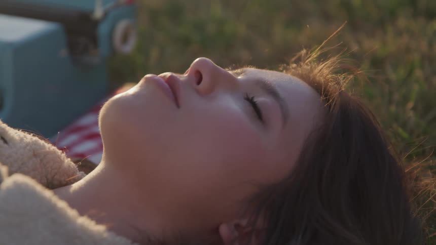 A woman smiles and closes her eyes as she lies in a field with a turquoise typewriter nearby