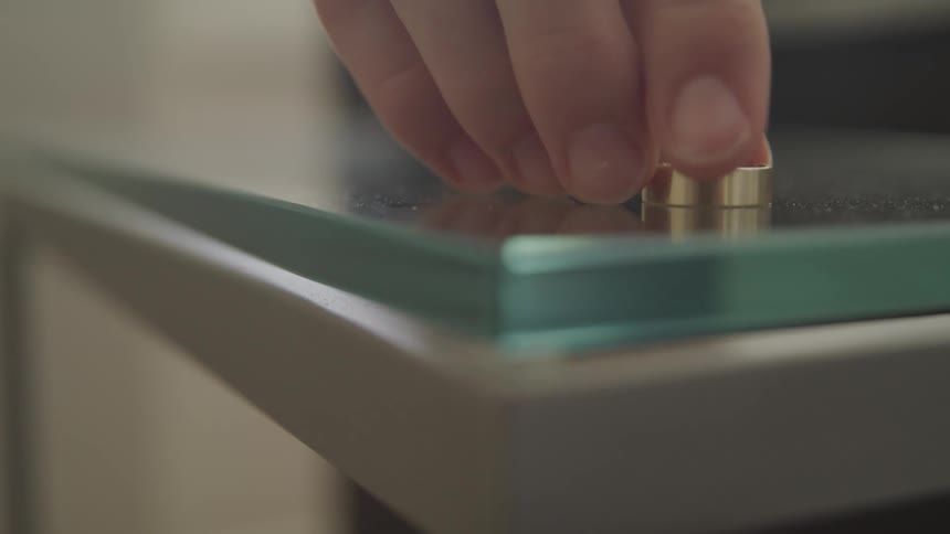A person places a smooth copper ring over a glass surface on a table