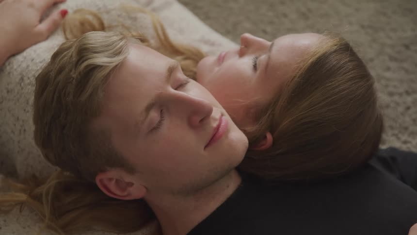 Young couple laying in the floor over a rug in a room with heads reclined on each other shoulders