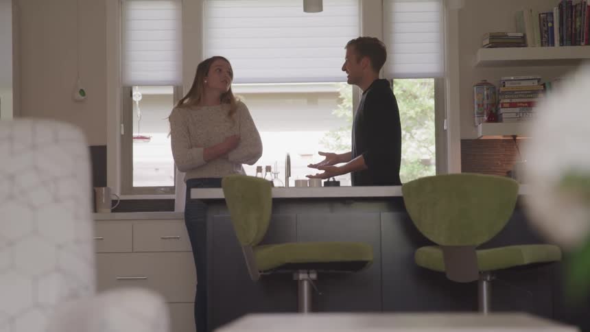 A man and woman stand in their home kitchen having an argument