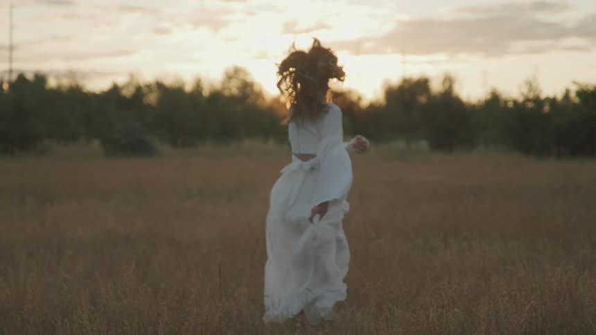A woman is running outdoors through the grass at dusk
