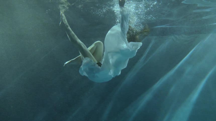 Woman in a white dress floating on the clear blue water in a pool