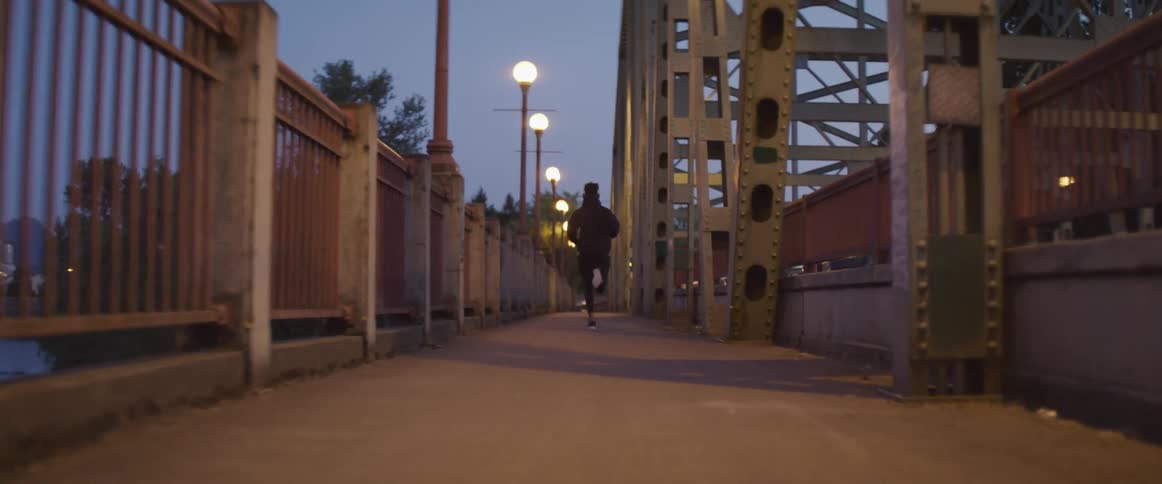 A man runs along a bridge on a sidewalk next to a roadway with vehicles