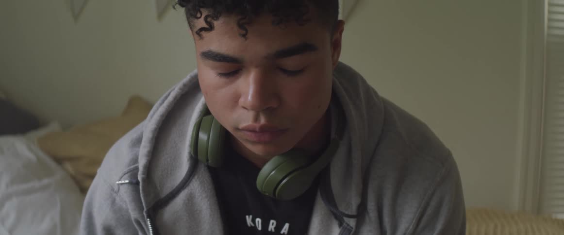 Young man wearing headphones sits with eyes closed on a bed in the bedroom at home