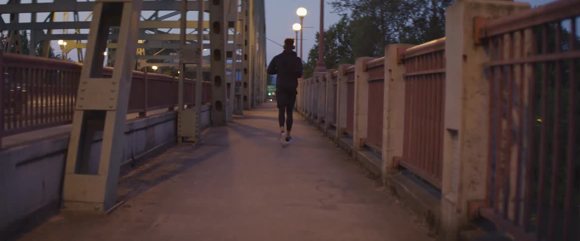 A man is jogging on a bridge at dusk