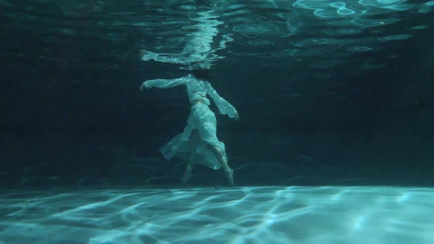 Under water footage of a woman in a dress standing in the water and rotating side to side