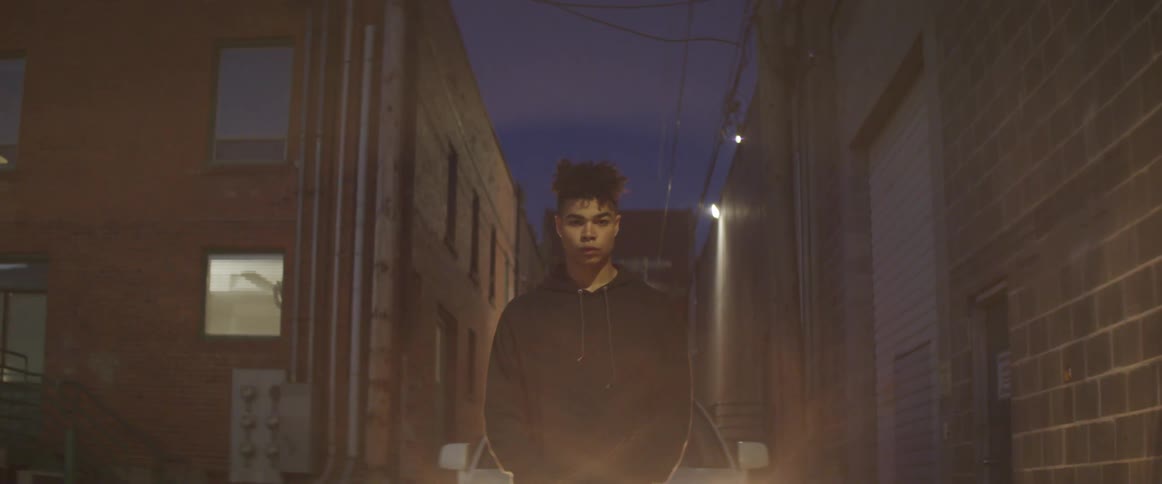 A teenage boy standing in an alley with police lights flashing around him