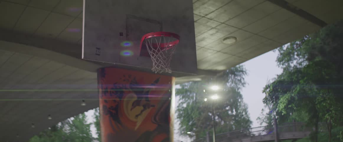 A basketball court with a pillar a bridge trees and the sky in the background