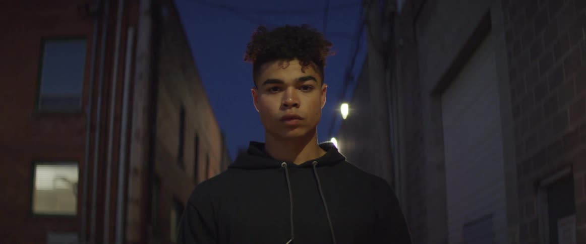 A man is standing in an alley with police lights shining on him