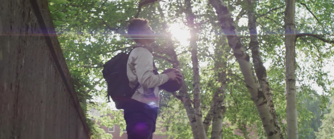A young man fidgets with a basketball while standing outdoors on a sunny day