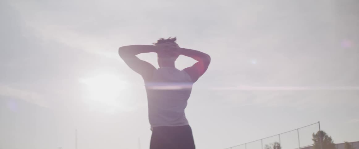 A person walking and putting their hands on their head with the sky clouds and trees in the background
