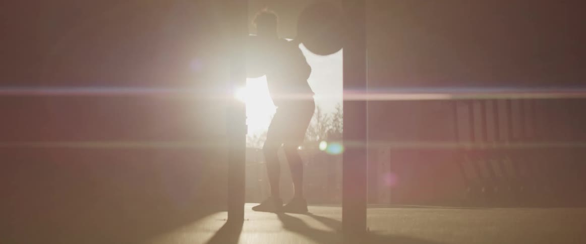 Man lifts weight bar in dim room back lit by sun through open doorway