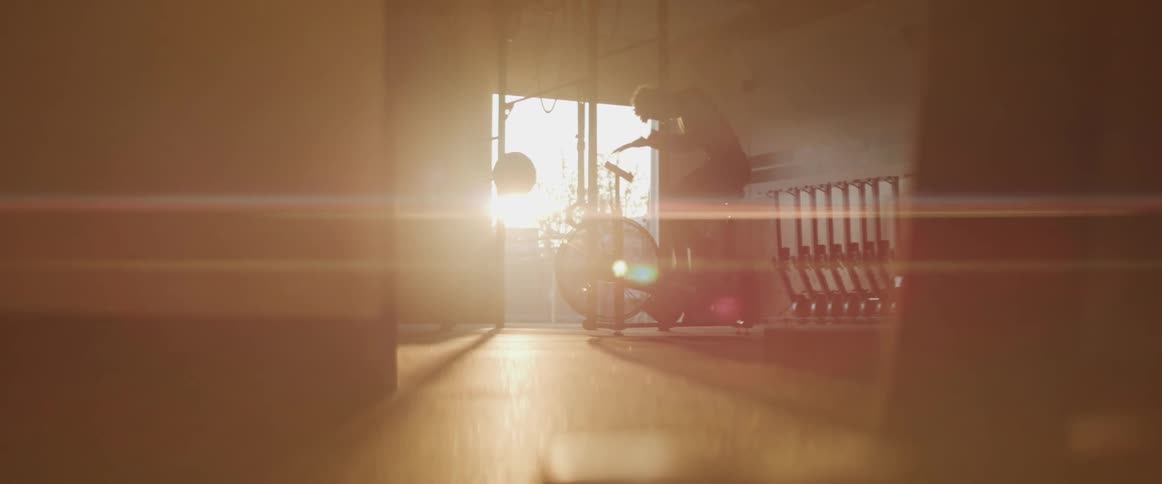 A man rides an exercise bike indoors during sunset