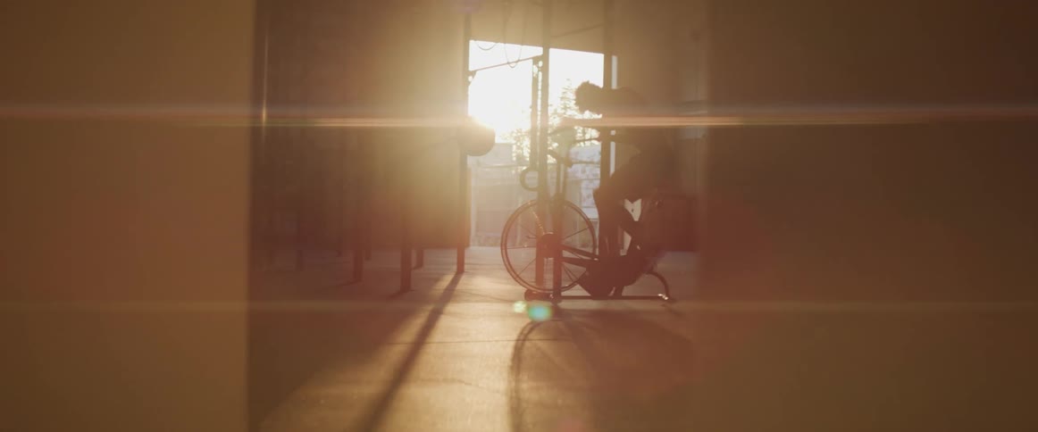 The sun shines through an open door as a teenage boy exercises on a stationary bike