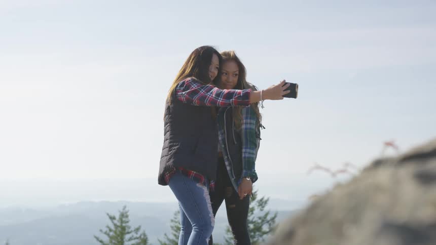 Women huddle close taking selfie standing with fog covered view behind them
