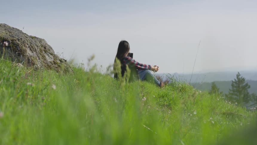 A teenage girl sits on a hill and looks at her cell phone