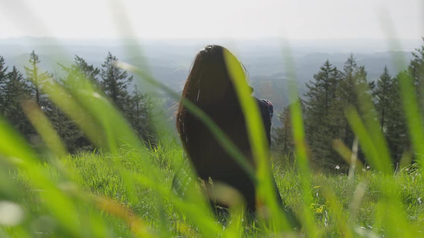 A woman is sitting outdoors and looking at the horizon