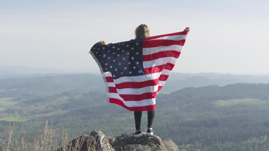 A woman is holding an american flag on the mountain top