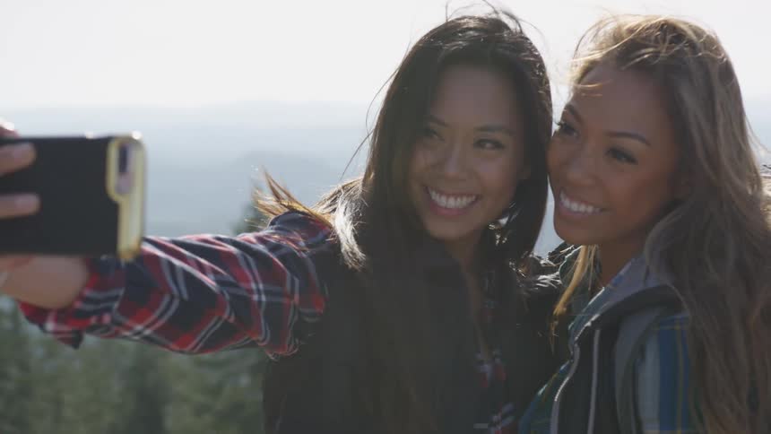 Two long haired woman taking a selfie together outdoors