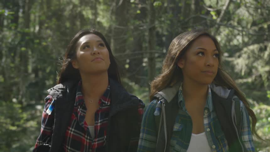 A pair of young women hike through a woodland together on a sunny day