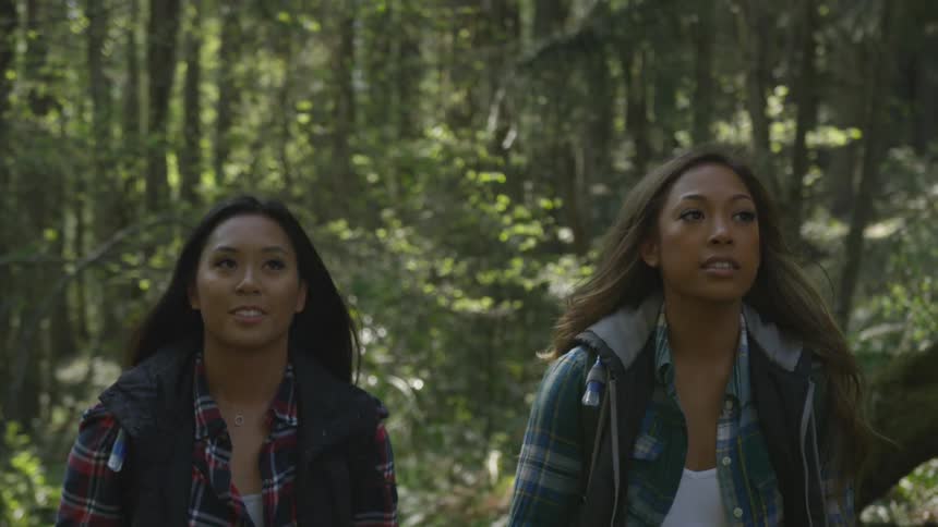A pair of women hike together through a forest during the day