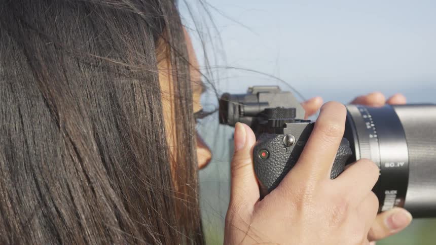 A young woman outside raises a camera to her eye