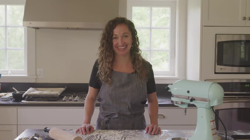 Female standing in front of kitchen counter after preparing cookies smiles and poses for a picture