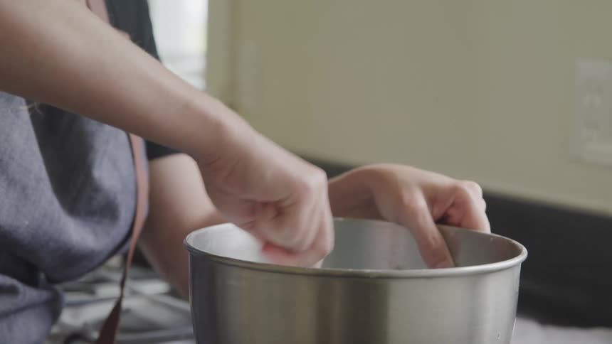 Woman stands in kitchen stirring contents of metal mixing bowl