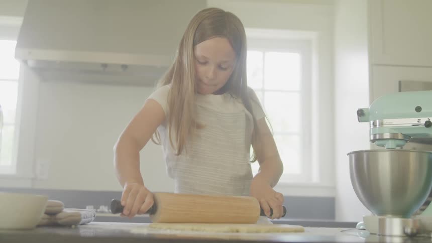 A young girl rolling dough in the kitchen