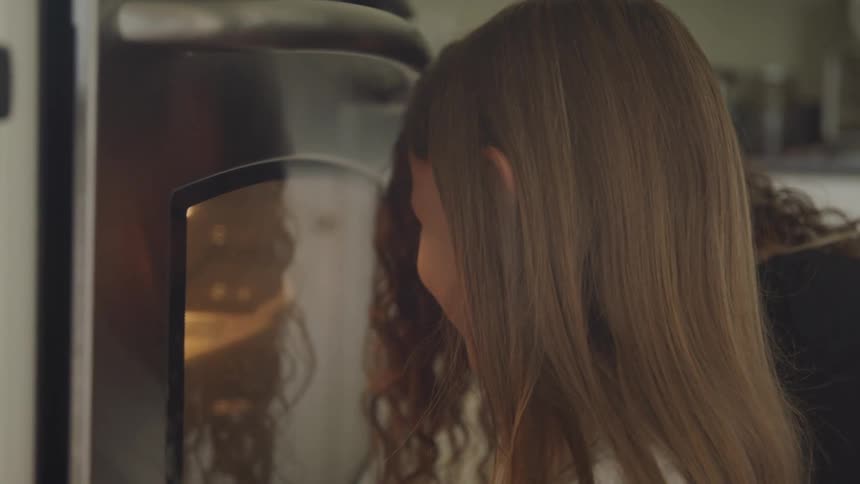 A girl and a woman look through the window of an oven as it bakes some food