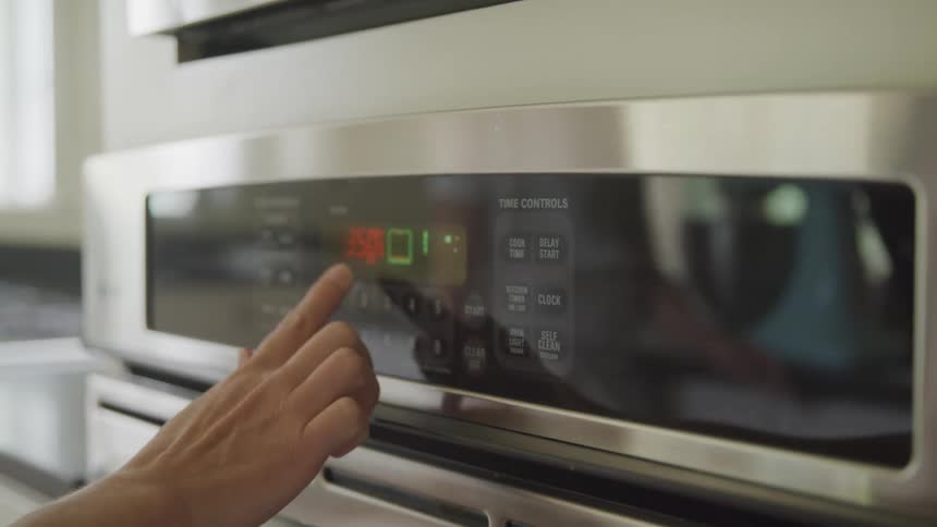 A person pushing buttons on a stainless steel oven in a kitchen