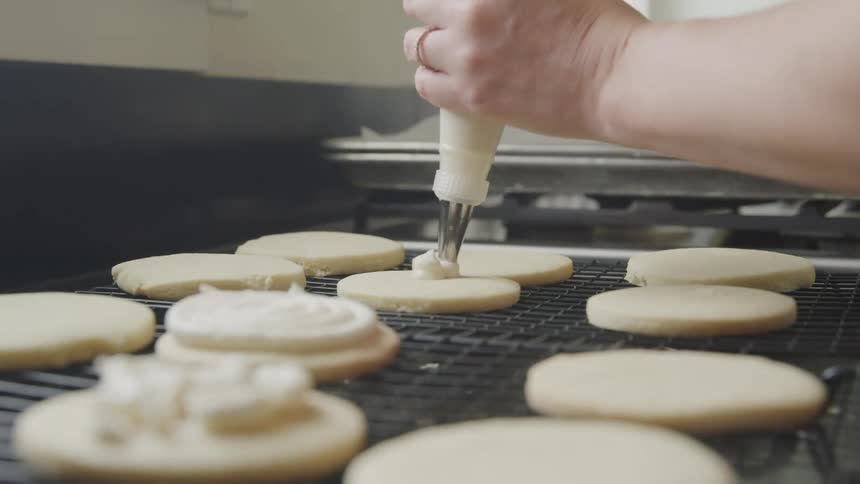 Person pipes frosting onto sugar cookies on cooling rack