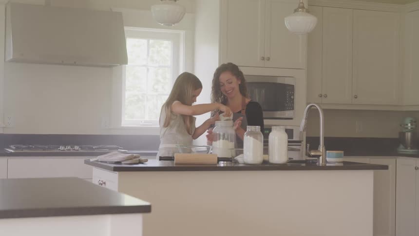 A mother and young daughter are in the kitchen with baking ingredients