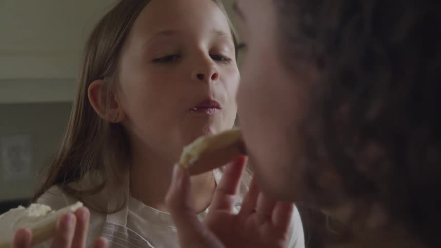 A mother and daughter eat cookies in the kitchen